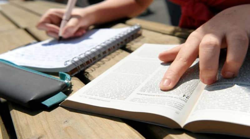 Mão escrevendo em caderno analisando Bíblia