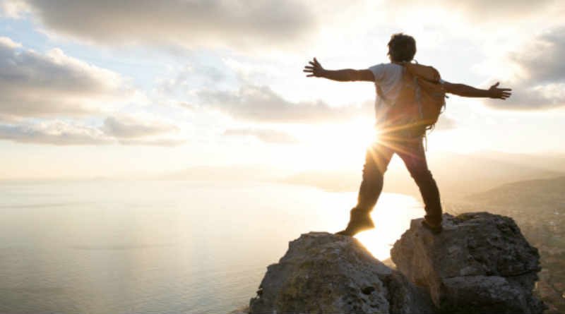 Jovem no topo de uma montanha vendo o horizonte vitorioso